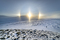 Three suns seem to hug the horizon in this otherworldly winterscape.