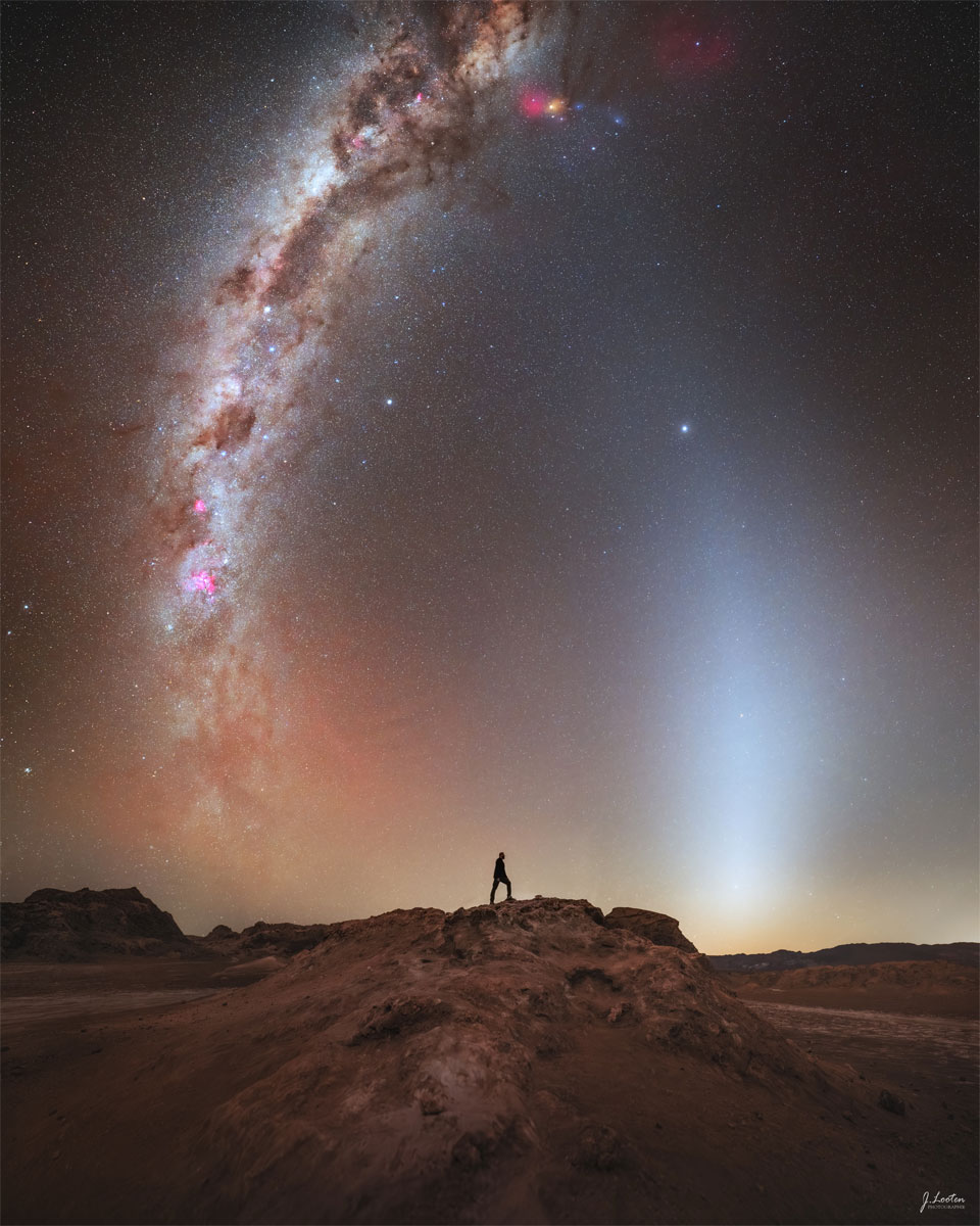 A distant person stands on a rocky landscape. Above is a
starry sky. Rising up from the horizon on either side of
the person are bright arching spires. 
Please see the explanation for more detailed information.