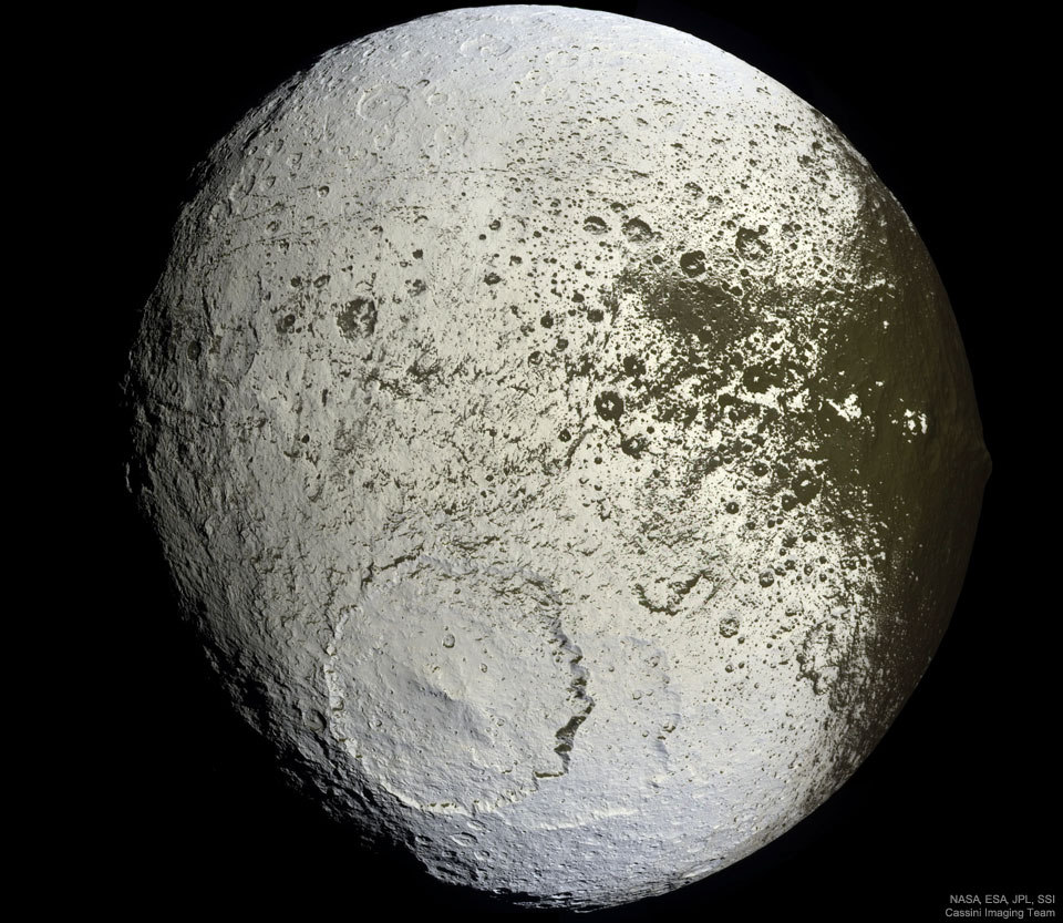 An unusually colored ball is shown against a 
dark background. The ball has numerous craters but
a very large cratered near the lower center. Much of
the ball is light colored, but around the right and
top it is green-brown, with a border area that seems
splattered. 
Please see the explanation for more detailed information.