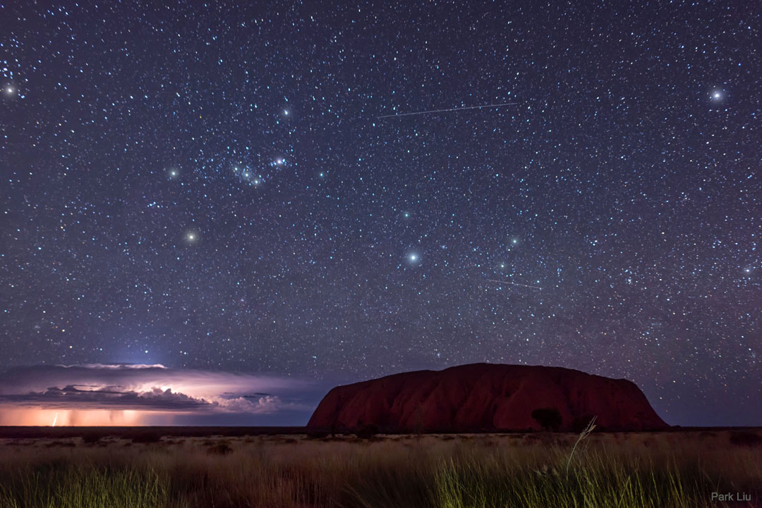 Una imagen de la roca Uluru en Australia frente a un rayo y la constelación de Orión.  Consulte la explicación para obtener información más detallada.