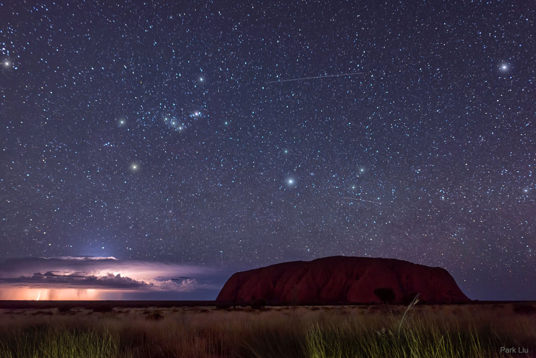 A picture of Uluru rock in Australia in front of lightning and the constellation of Orion.   Please see the explanation for more detailed information.