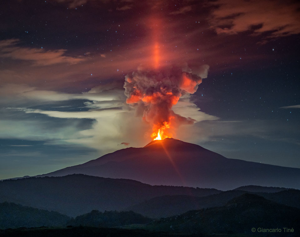 La muestra ilustración un pilar de luz roja en la noche sobre el monte Etna, un volcán en erupción en Italia.  Consulte la explicación para obtener información más detallada.