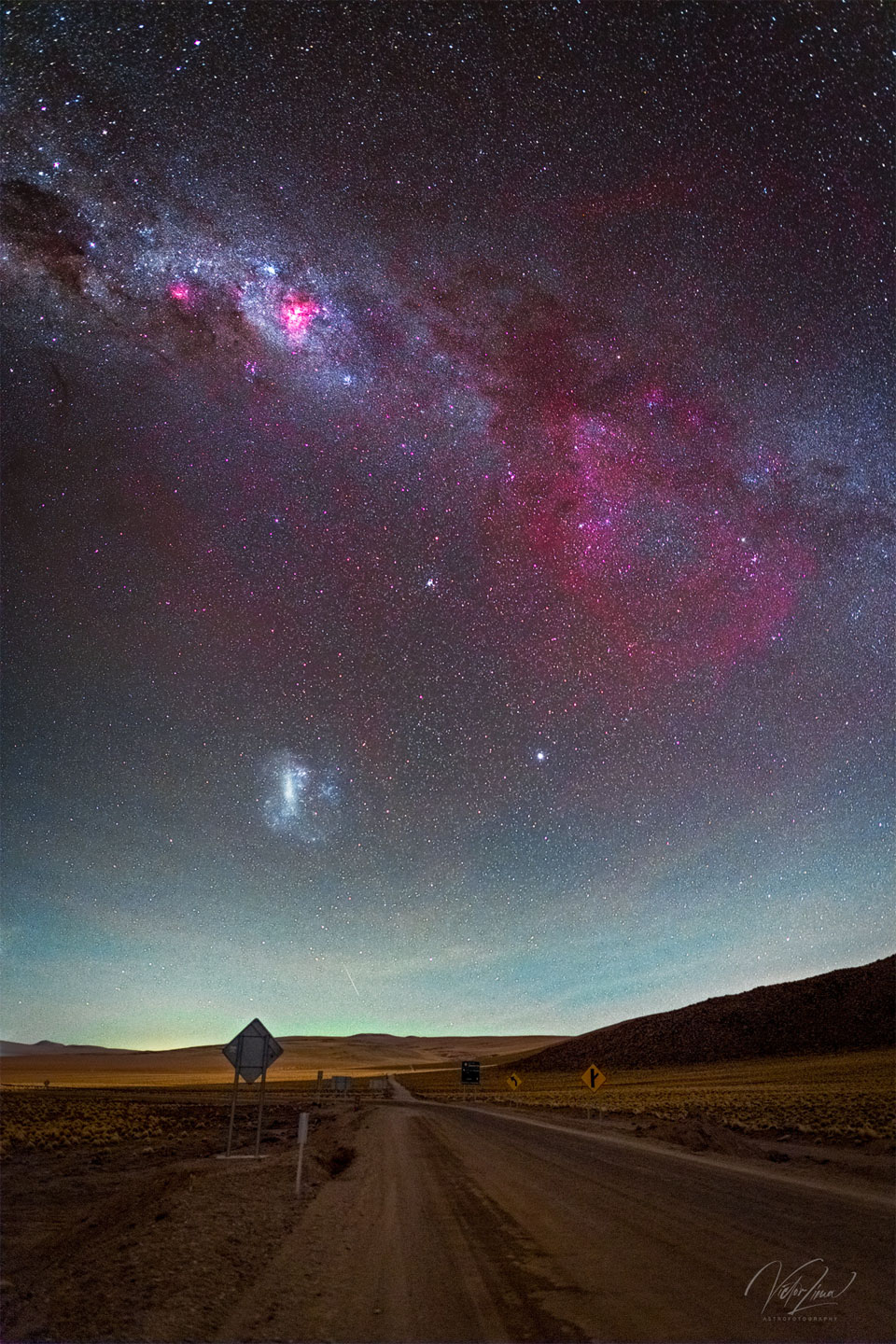 The featured image shows a grand skyscape with a   brown desert road in the foreground and a sky containing  the Milky Way galactic band complete with a large red   glow on the right which is the dim Gum Nebula. The  LMC galaxy is also visible.   Please see the explanation for more detailed information.