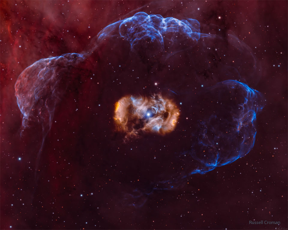 The featured image shows a star inside a symmetric but complex
and multi-colored nebula which is all surrounded by a faint blue nebula.
Please see the explanation for more detailed information.