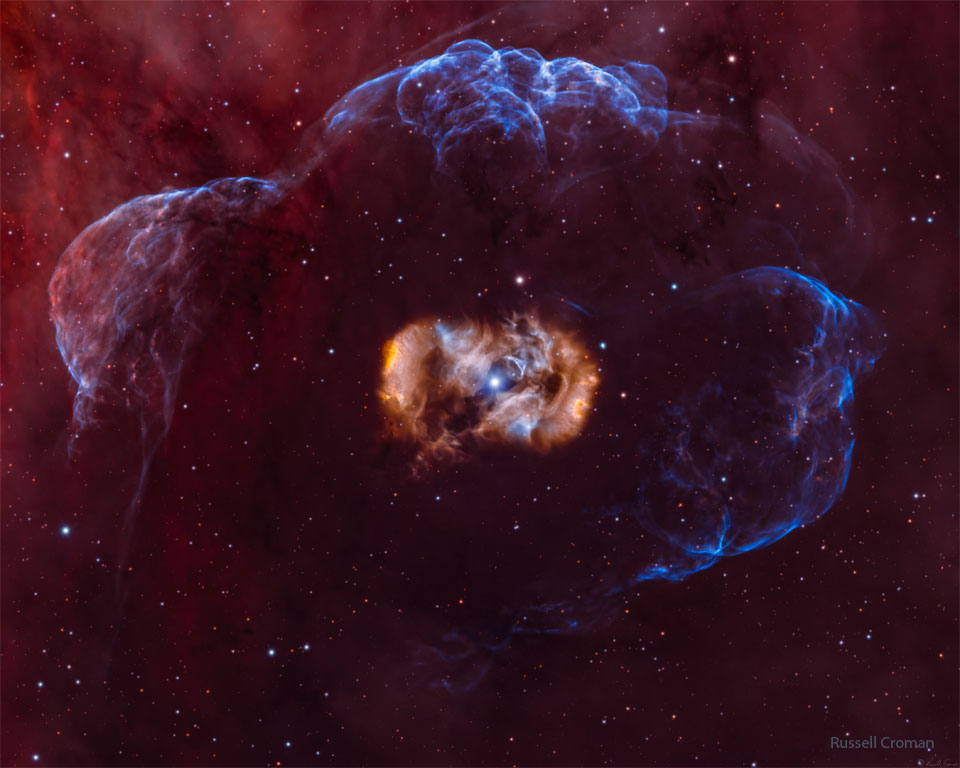 The featured image shows a star inside a symmetric but complex  and multi-colored nebula which is all surrounded by a faint blue nebula.  Please see the explanation for more detailed information.