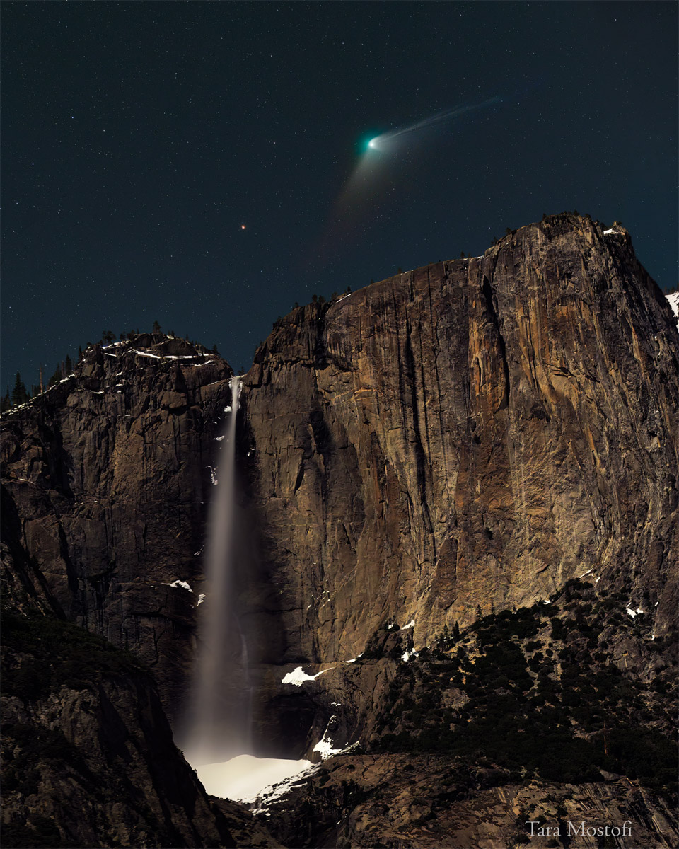 A comet with a green head and extended tails is seen
above a high water fall. In the night sky field just above
the falls, an orange dot -- the star Kochab -- is visible.
Please see the explanation for more detailed information.
