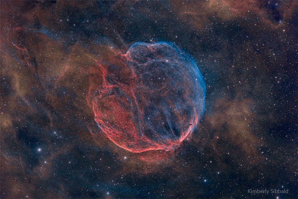 A nearly spherical but stringy nebula is shown against
a starry background. The nebula is colored blue and red. 
Please see the explanation for more detailed information.