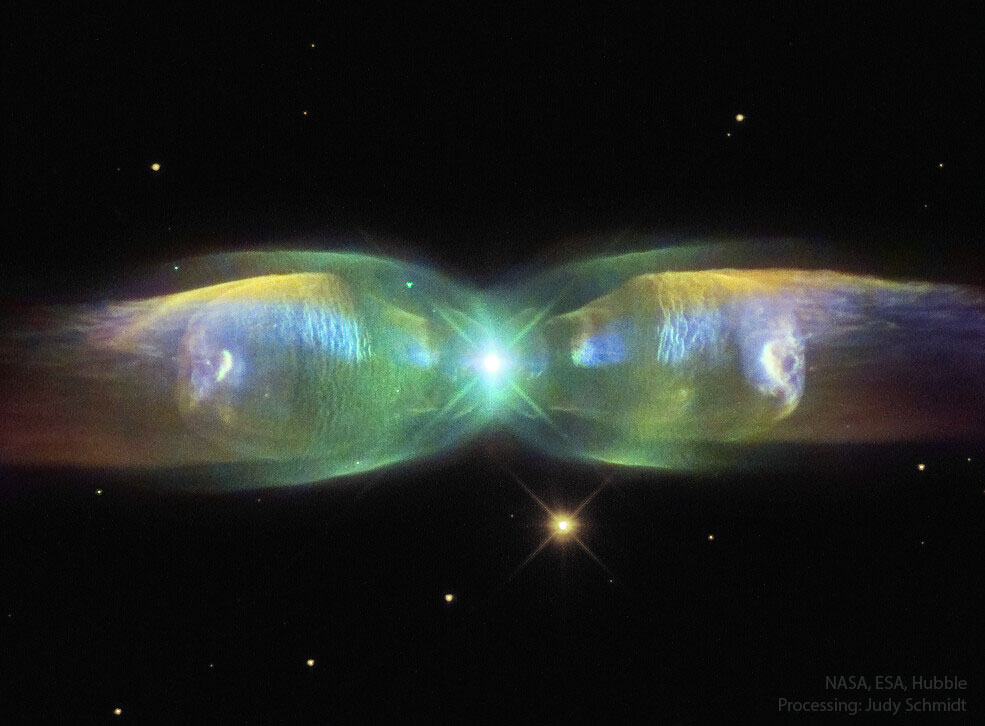 An elongated colorful nebula is shown elongated
horizontally and pinched in the middle. In the very
center is a bright source.
Please see the explanation for more detailed information.