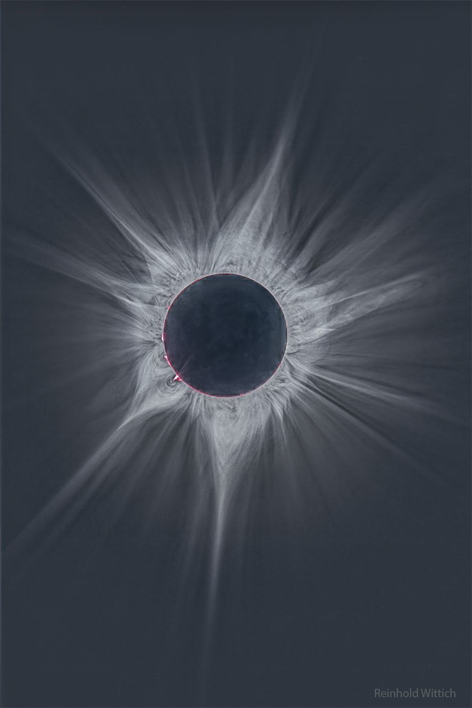 A deep image of the Sun's surrounding corona during the April 2023 total solar eclipse. The central disk is dark and many bright and complex rays are seen extending out. A few hot pink filaments can be seen just around the Sun's edge. Please see the explanation for more detailed information.