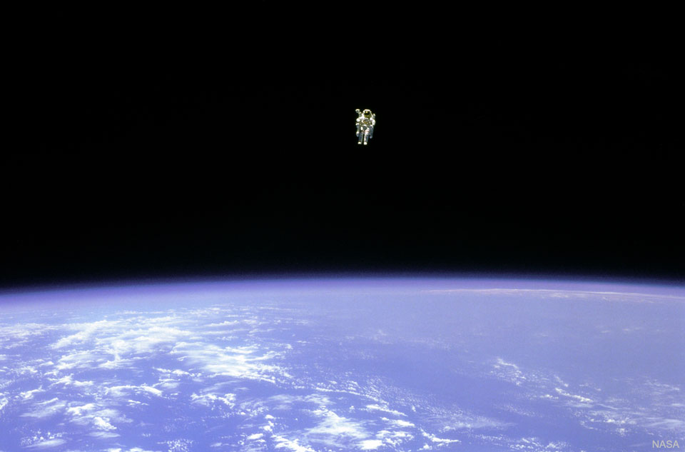 An astronaut is seen hovering over the Earth. In the 
top part of the image, the astronaut is seen against the 
darkness of space. In the lower part of the image, the
Earth is bright blue with white clouds.  
Please see the explanation for more detailed information.