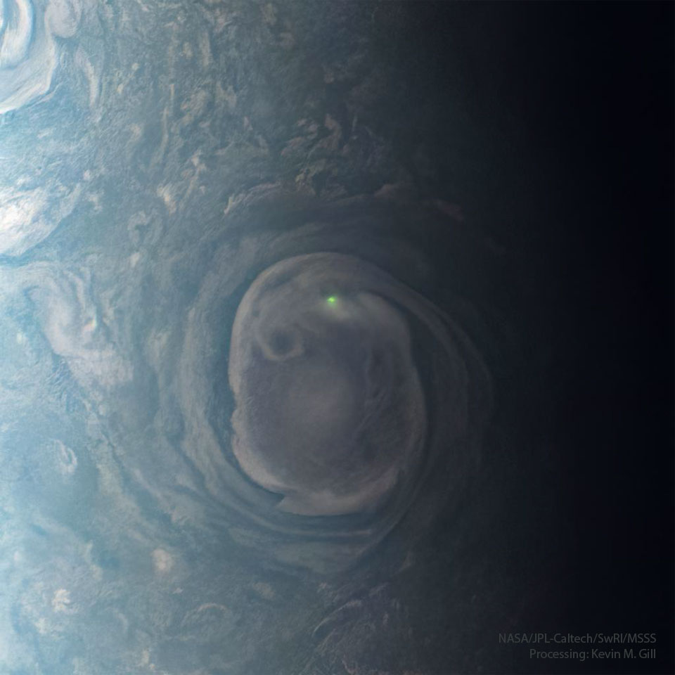 A large swirling cloud on Jupiter is shown with a bright green
spot near its top. The cloud is surrounded by other less descript 
parts of Jupiter's upper atmosphere.
Please see the explanation for more detailed information.