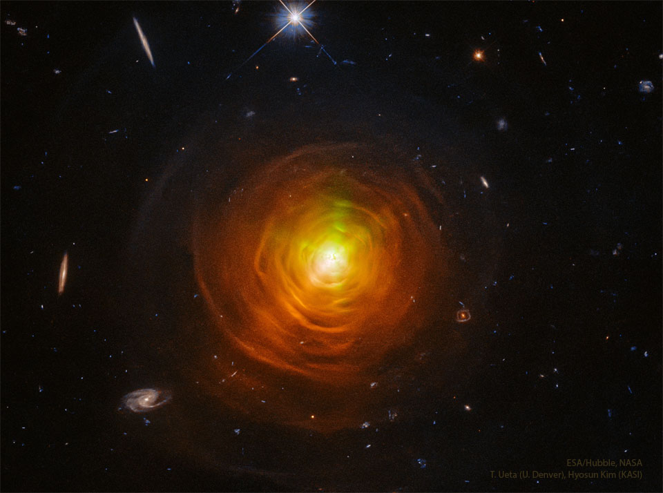 A star surrounded by orange shells and arcs sit in the center of
a dark starfield. Galaxies from the distant universe can be seen around
the edges.
Please see the explanation for more detailed information.