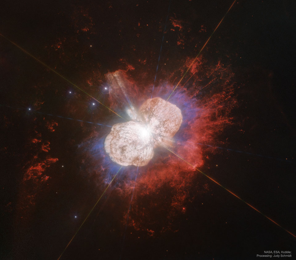 A Hubble image of the gas and dust surrounding the star Eta Carinae 
is shown. The nebula has two distinct light-colored lobes, surrounded by
red glowing gas. 
Please see the explanation for more detailed information.