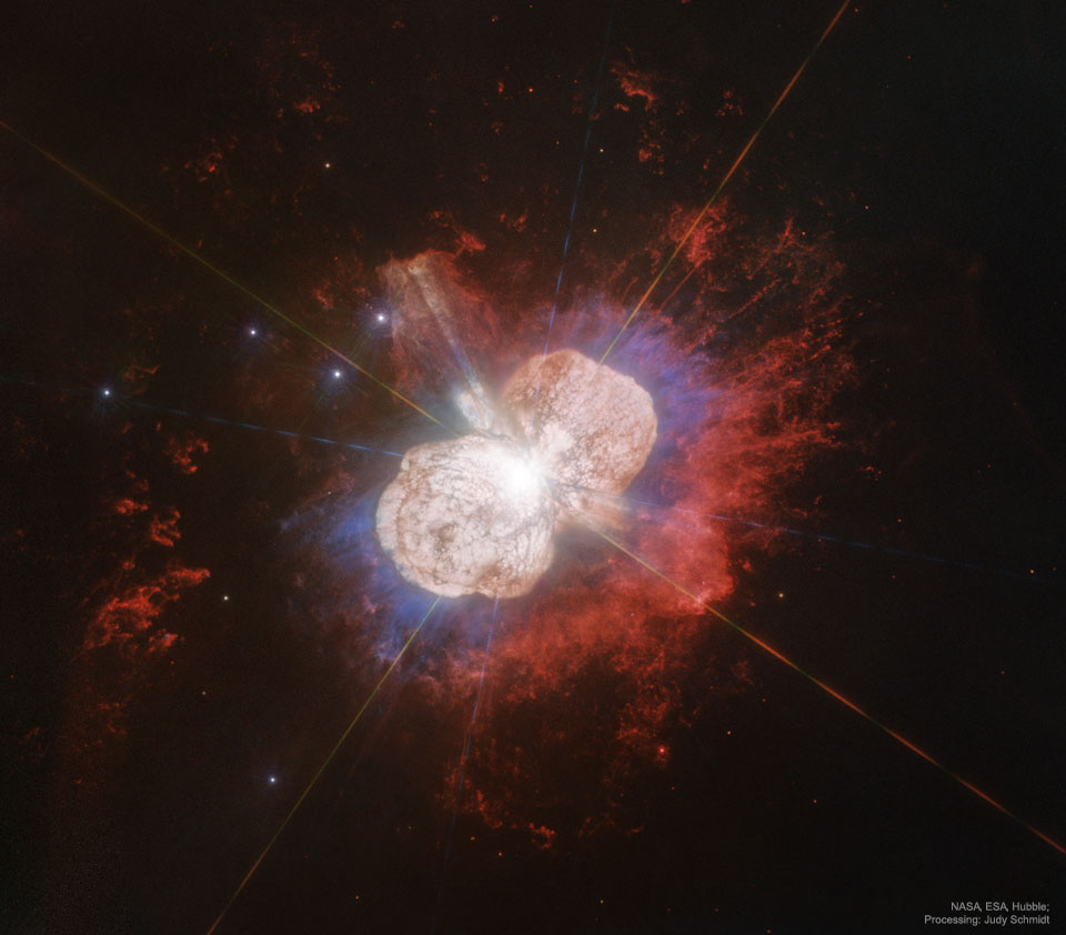 A Hubble image of the gas and dust surrounding the star Eta Carinae is shown. The nebula has two distinct light-colored lobes, surrounded by red glowing gas. Please see the explanation for more detailed information.