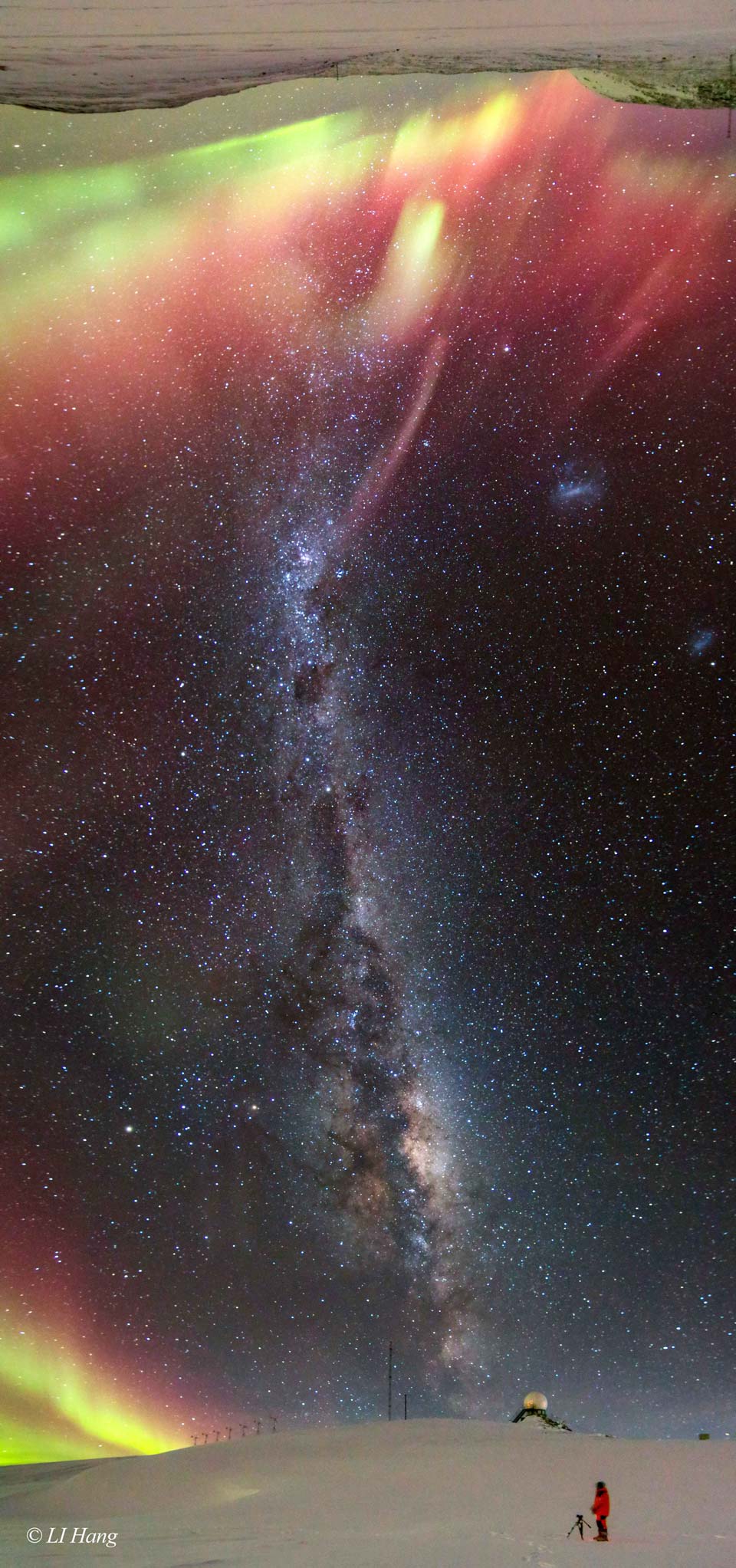 A long vertical image shows a band of the night sky from
horizon at the bottom to the opposite horizon -- at the image top.
A person stands on a snow covered landscape with the central
band of the Milky Way running between horizons. Each horizon
is lit by red, yellow, and green auroras.
Please see the explanation for more detailed information.