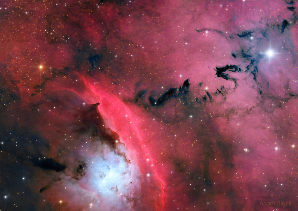 A busy star formation region is shown highlighted by red glowing clouds
and dark ominously-shaped dust.
Please see the explanation for more detailed information.