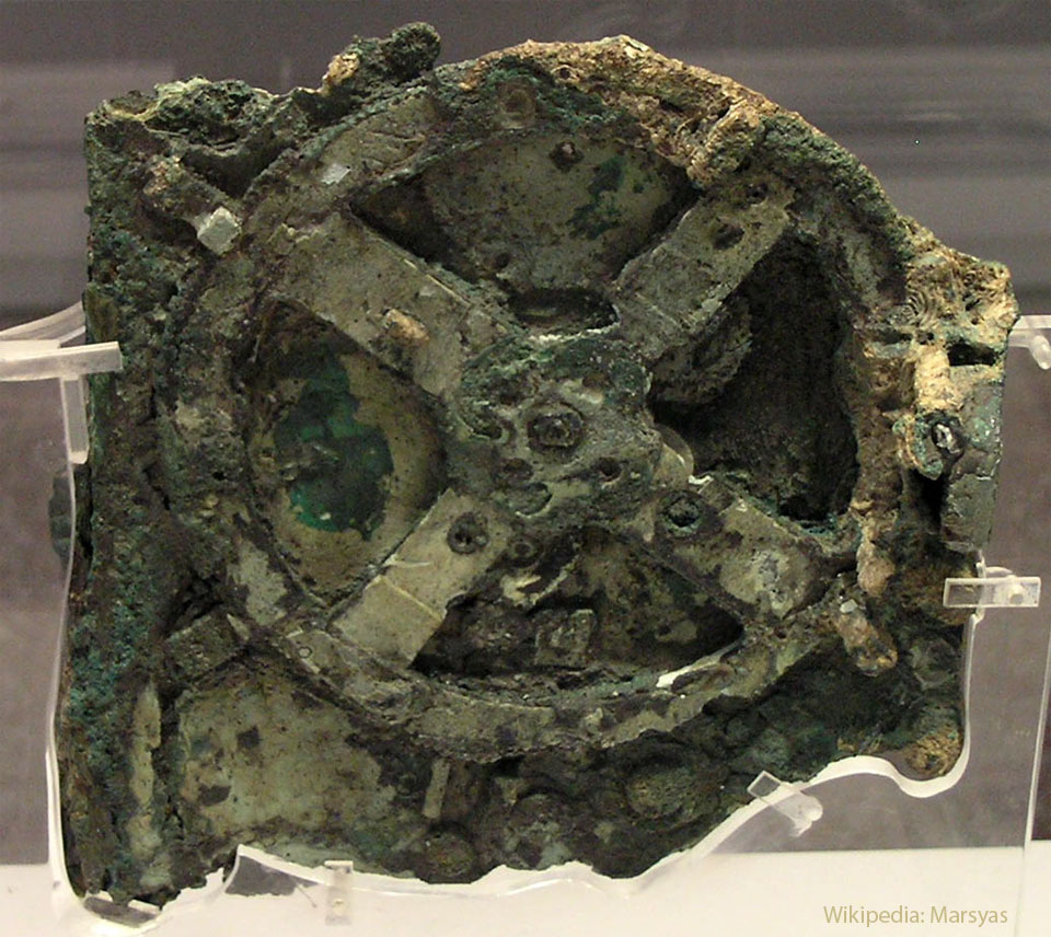 An old and corroded mechanism is shown fronted by a large
wheel. The mechanism has patches of tan and brown color but
it is mostly green. 
Please see the explanation for more detailed information.