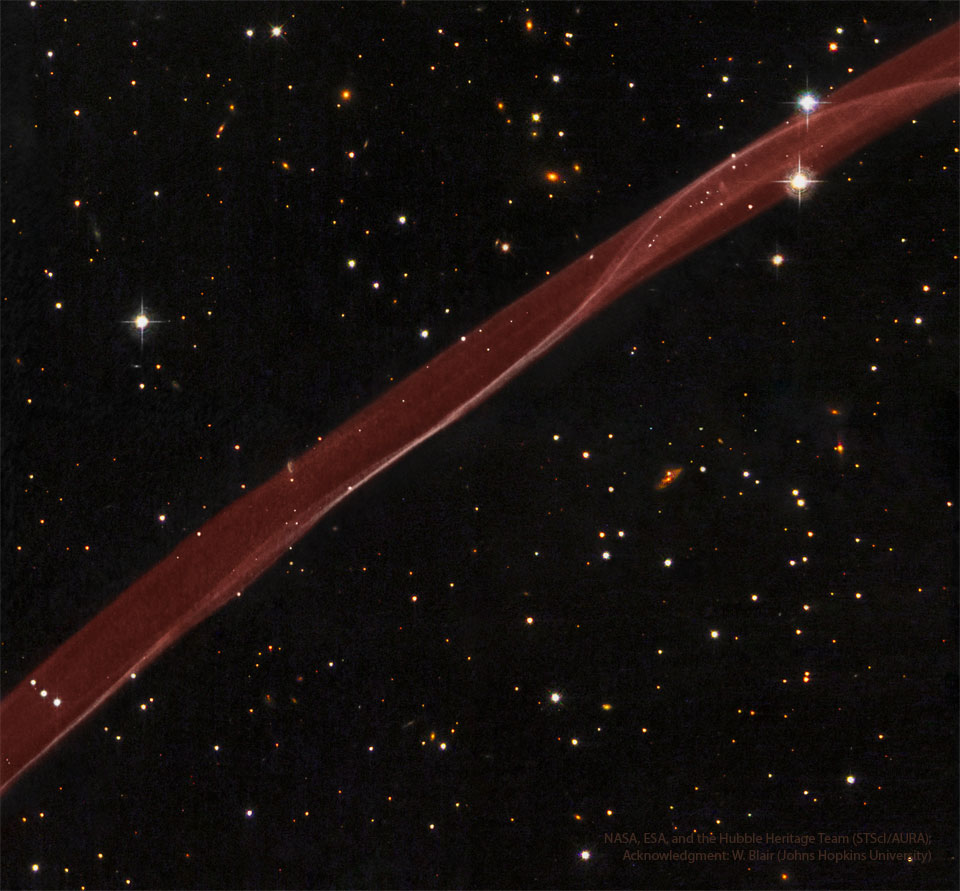 A thick transparent ribbon of red gas runs from the lower left to
the upper right. A dark starfield with stars and galaxies surrounds the 
bright red ribbon.
Please see the explanation for more detailed information.