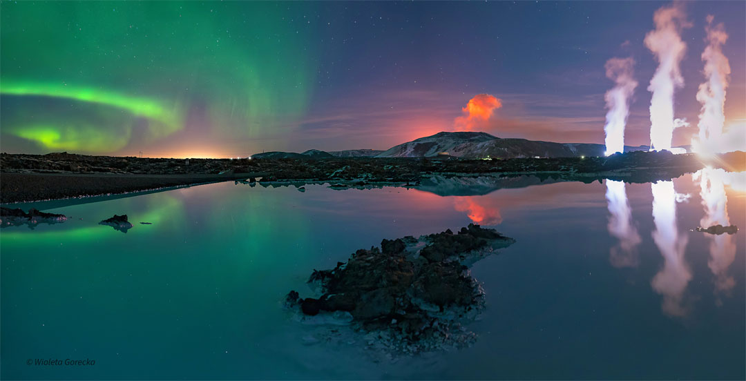 A body of water is seen in front of a night sky. The  water reflects the sky. In the sky, on the right are green  aurora. In the center is an orange plume. On the right  are three while plumes.   Please see the explanation for more detailed information.