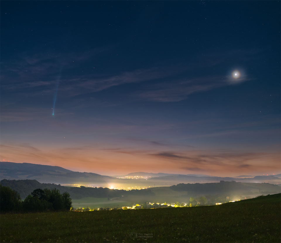 A scenic and hilly landscape is shown just before sunrise. 
On the left is Comet Nishimura near the horizon with a long tail
fading off toward the top of the frame. On the right is a bright spot
that is Venus. The sunrise sky is dark blue at the top but morphs
into tan at the horizon, while the foreground hills are green.
Please see the explanation for more detailed information.