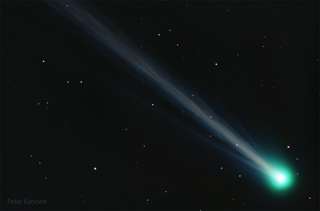 A comet is shown with its green coma on the bottom right  and a long and structured ion tail flowing diagonally across   the image toward the top left.  Please see the explanation for more detailed information.