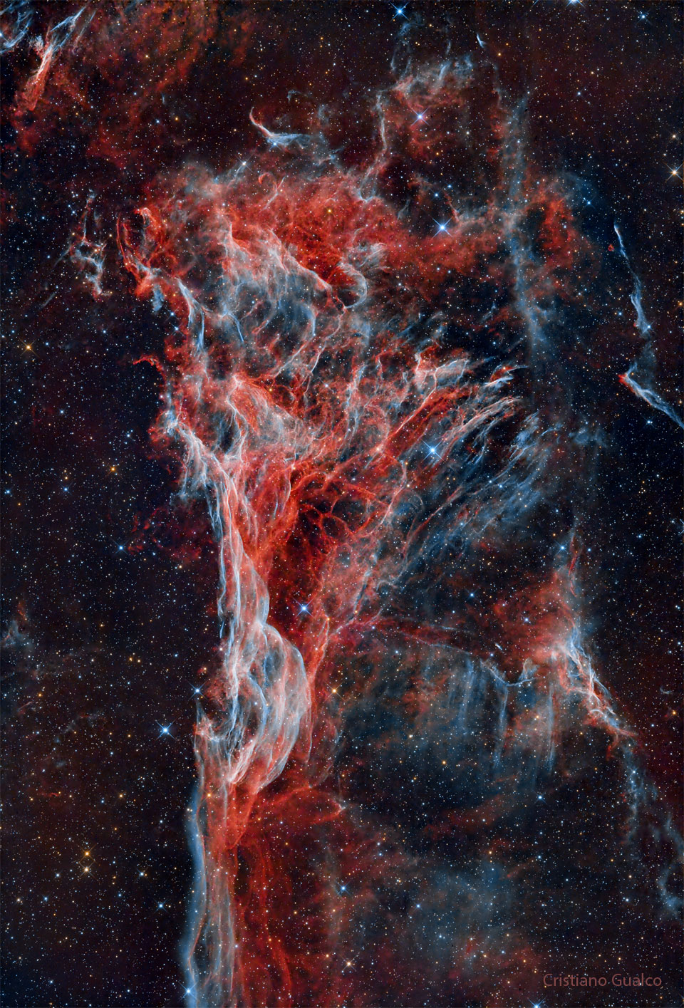 A nebula consisting of blue and red wisps starts 
thin at the image bottom but expands into a triangle
at the image top.
Please see the explanation for more detailed information.