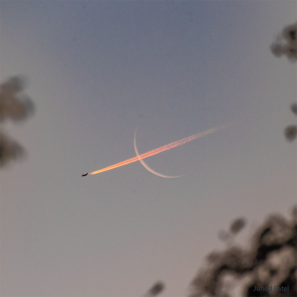 A thin crescent moon is shown with a bright red 
contrail going through it, right to left. 
Please see the explanation for more detailed information.