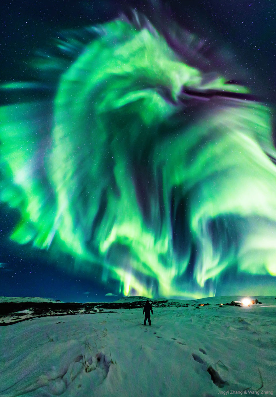 A person stands on snow and looks up at a starry sky.
In the sky is a large green aurora that resembles a dragon.
Please see the explanation for more detailed information.