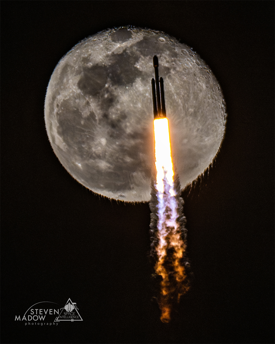 A rocket is pictured ascending during launch. 
A nearly full moon is behind it. The rocket exhaust,
itself visible, causes the bottom of the Moon to appear
unusually rippled.
Please see the explanation for more detailed information.