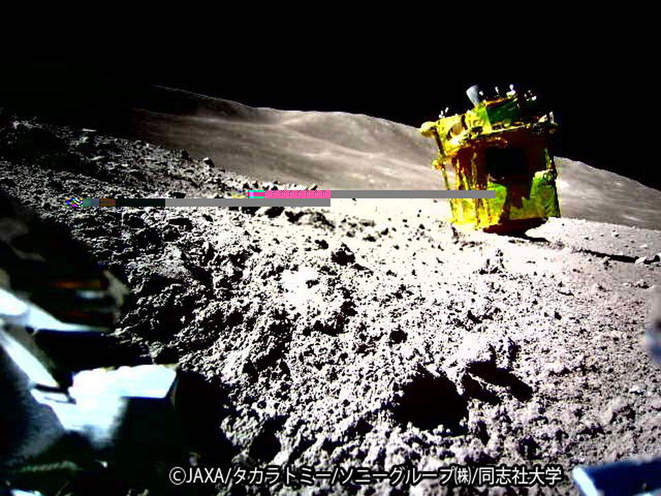 The lunar surface is shown with a box-like gold-colored
machine in the middle. A close inspection of the machine 
reveals that its thrusters are at the top, so it is on its
side. The background sky is dark. Two horizontal lines 
are an artifact of the digital imaging and
not part of the lunar landscape.
Please see the explanation for more detailed information.