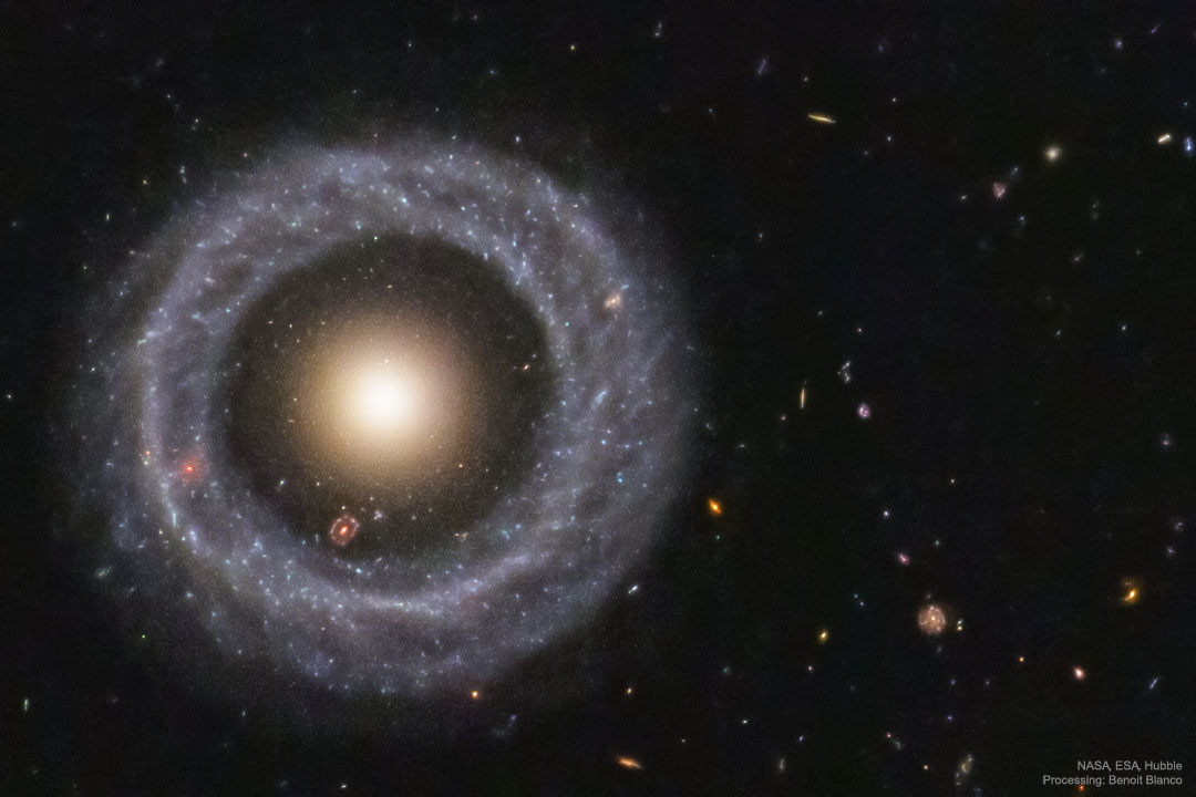 A nearly perfect circular ring of blue stars is seen
against a dark field of small background galaxies.
In the center of the ring is a ball of yellow stars.
Please see the explanation for more detailed information.