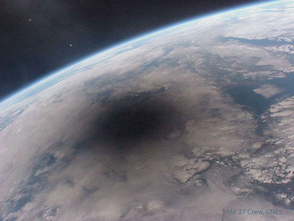 Part of the the Earth is pictured with blue seas and
white clouds. On the upper left is a deep space dark background.
On the Earth a large dark spot is apparent. Please see the explanation for more detailed information.