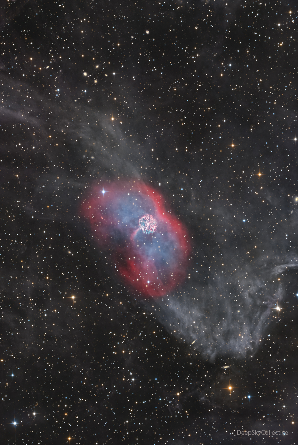 A faint nebula runs vertically in the image. In the
center is a red envelope surrounding diffuse blue emission.
In the center is a bright multicolored nebula that is 
nearly circular. 
Please see the explanation for more detailed information.