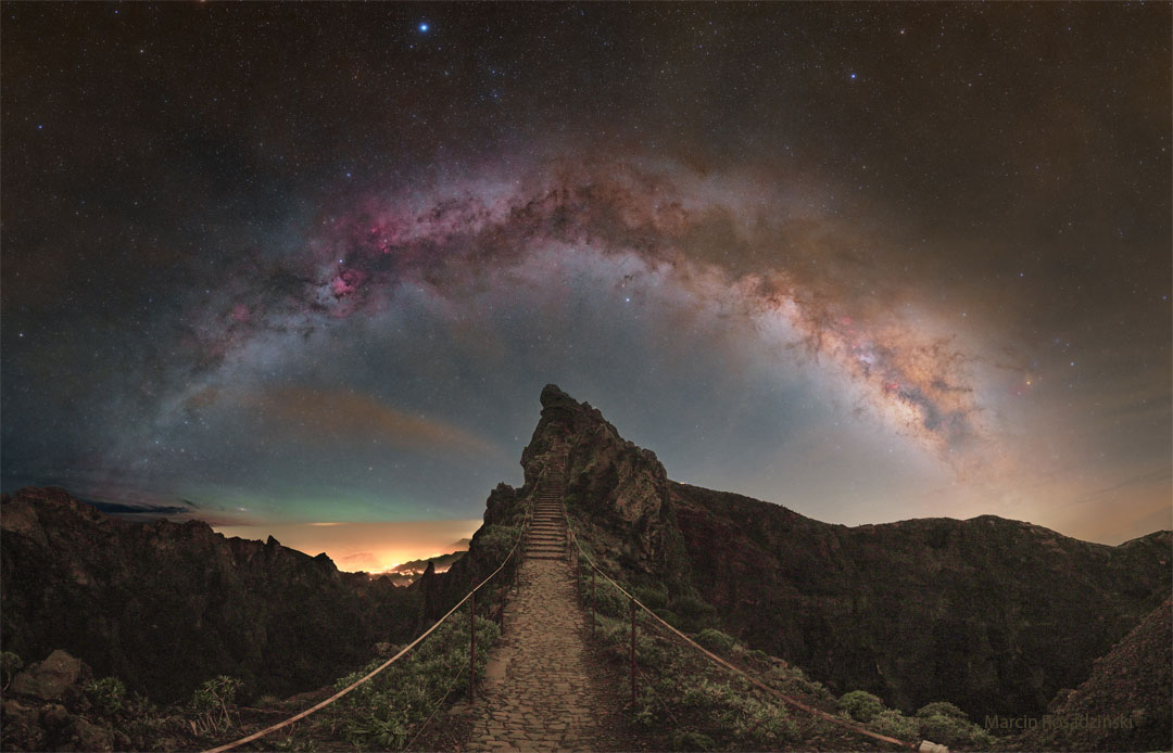 A star filled sky shows the arch of the central band of
our Milky Way galaxy across the top of the image. In the foreground
is a rocky landscape with a hill ahead and a pathway that leads
to stairs up that hill.
Please see the explanation for more detailed information.