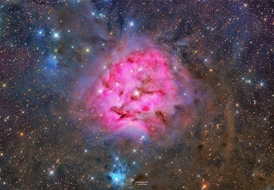 A red emission nebula is shown against a busy starfield   with many dark dust filaments near the nebula's center.   Near the bottom of the image is a smaller blue reflection   nebula.   Please see the explanation for more detailed information.