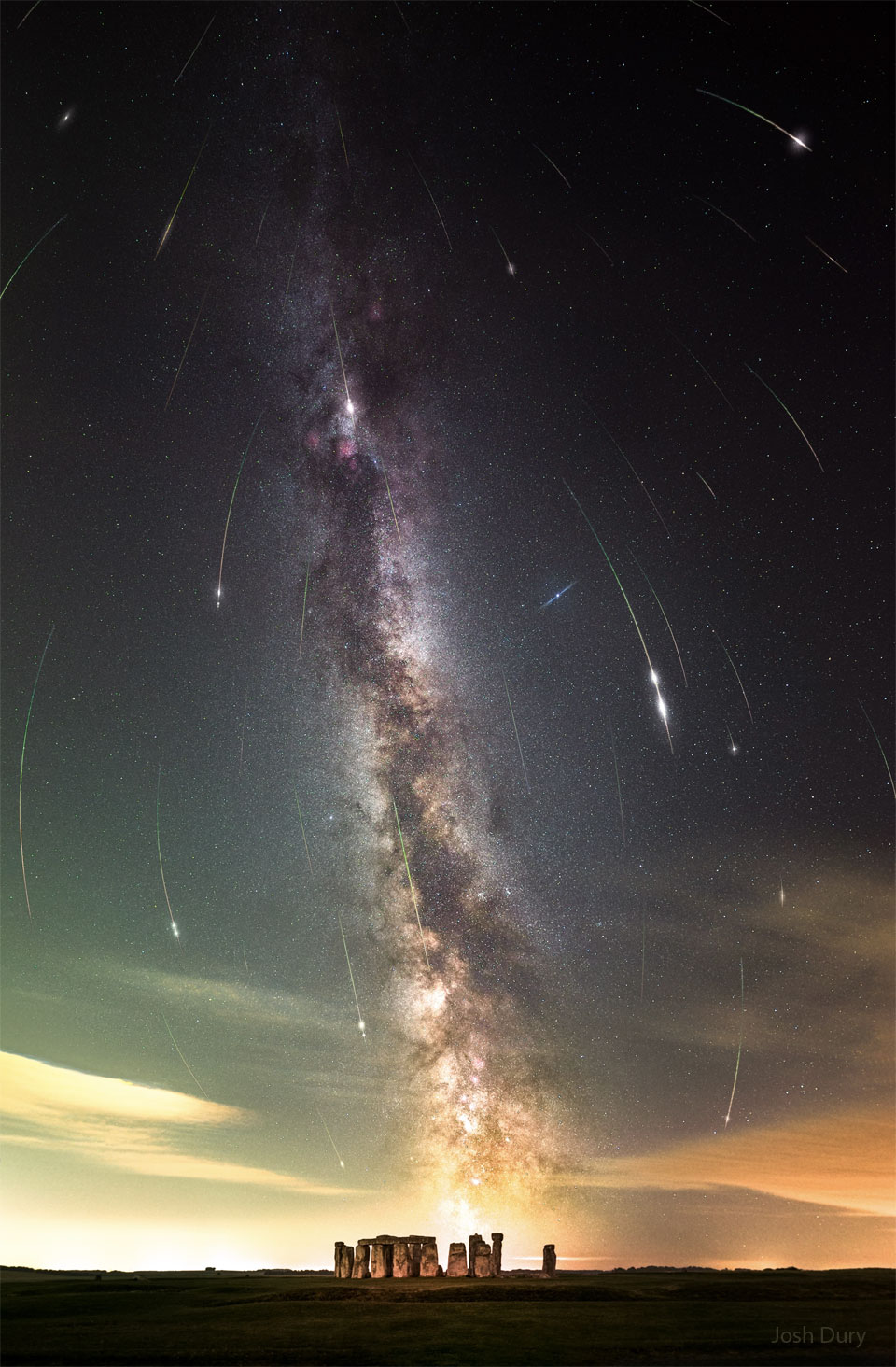 A night sky filled with stars and the band of our Milky  Way galaxy is shown also filled with many streaks. The short  streaks are all coordinated and together indicate a flow  from the top of the image to the bottom. In the foreground  at the bottom of the frame is Stonehenge.  Please see the explanation for more detailed information.