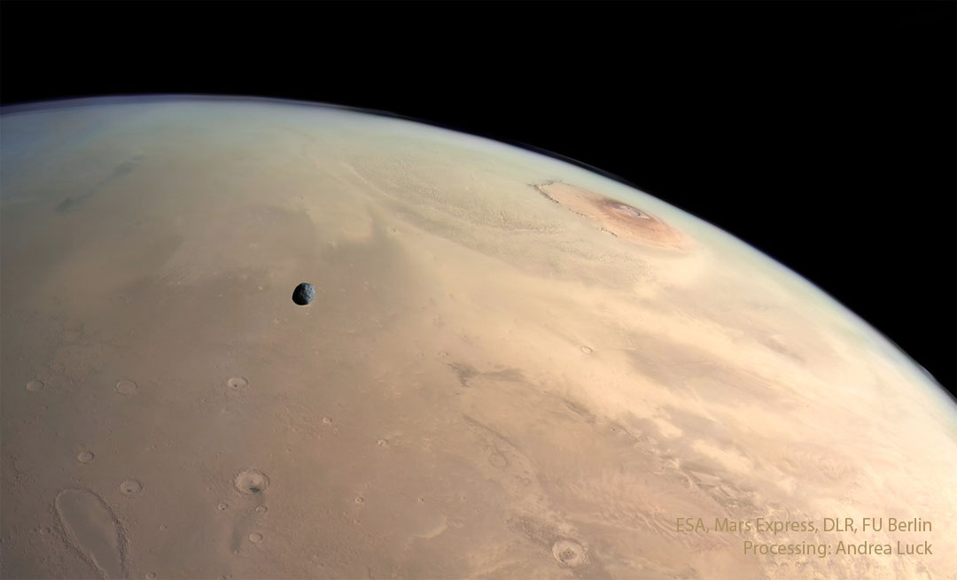 A panoramic view of the surface of Mars. Several landforms are   visible including craters and volcanos. A small dark moon is superposed  in front of part of the surface.   Please see the explanation for more detailed information.