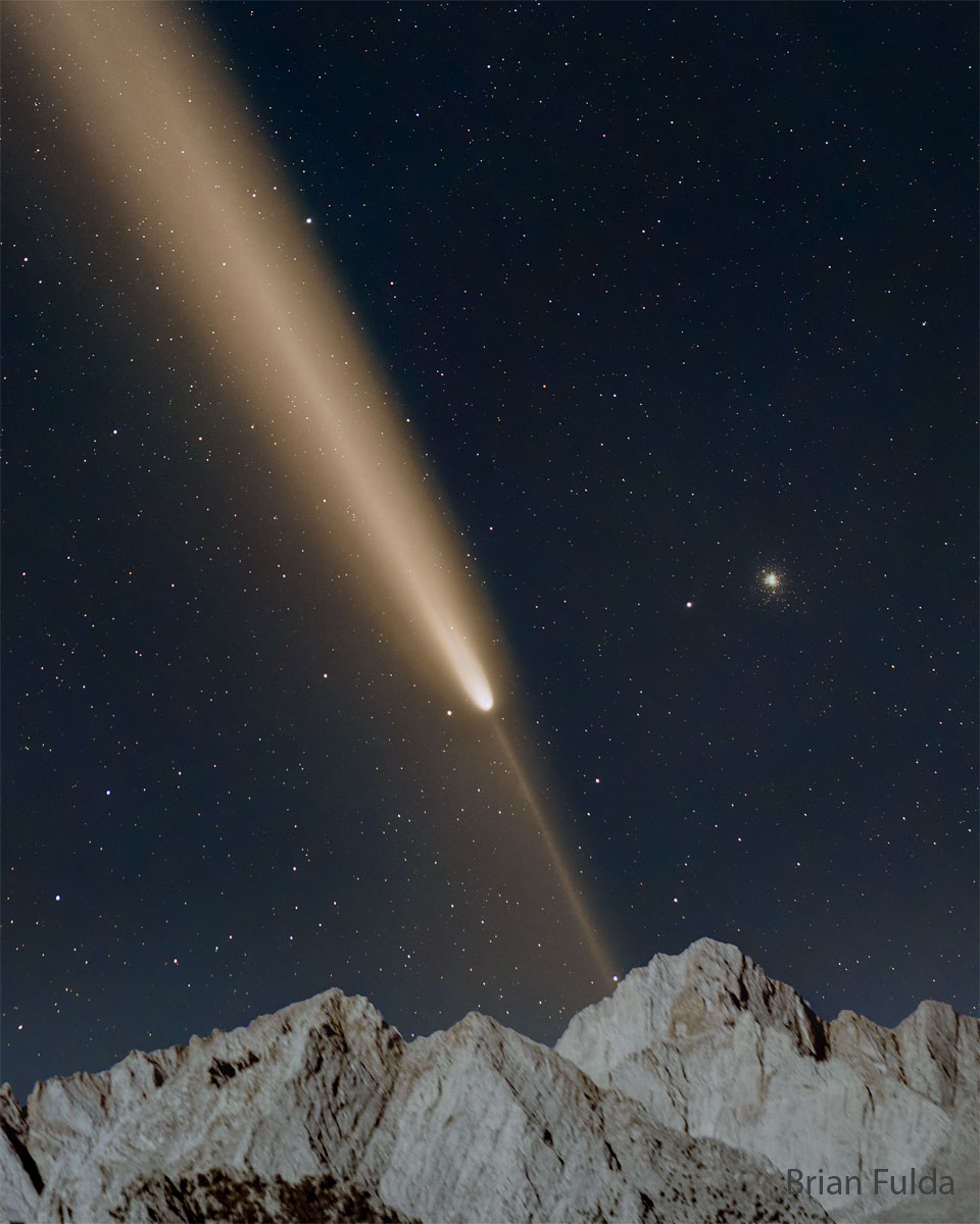 A starfield is shown with a bright comet. The main  tail of the comet points diagonally to the upper left, while  a thin anti-tail points to the lower right. Mountain peaks  are visible at the bottom in the foreground.   Please see the explanation for more detailed information.