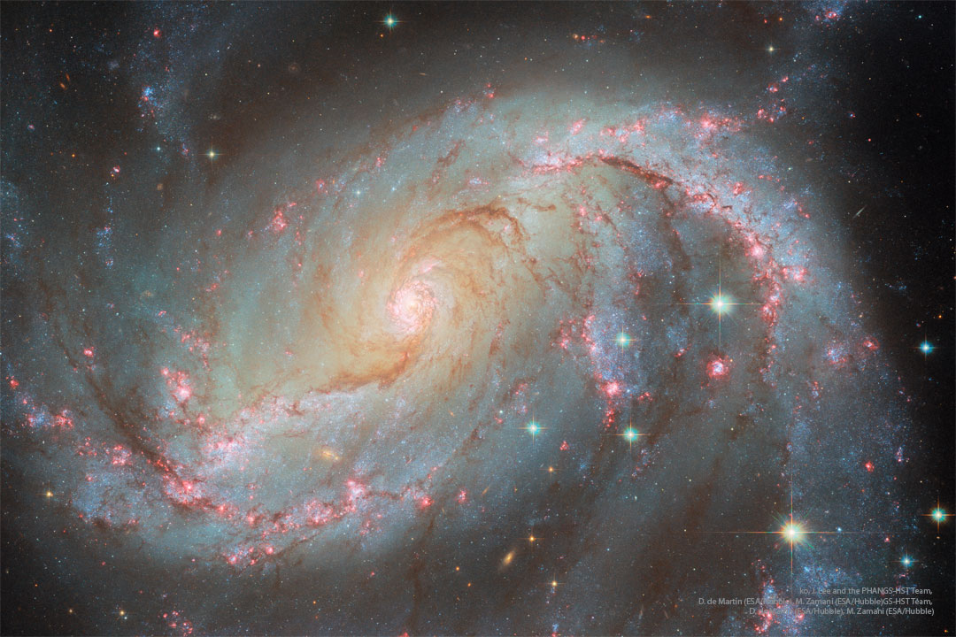 A spiral galaxy is shown in great detail. Visible   are blue star clusters, red nebulas, and brown dust  in a spiral pattern around the image and galaxy center.  Please see the explanation for more detailed information.