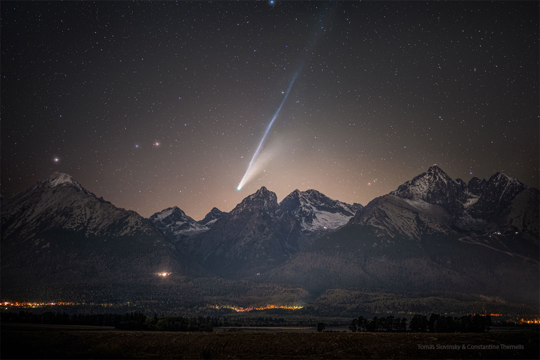 A mountain range is shown in the foreground with a
bright comet visible above it. The comet shows tails
that are long and bright with the longer tail appearing
light blue. 
Please see the explanation for more detailed information.