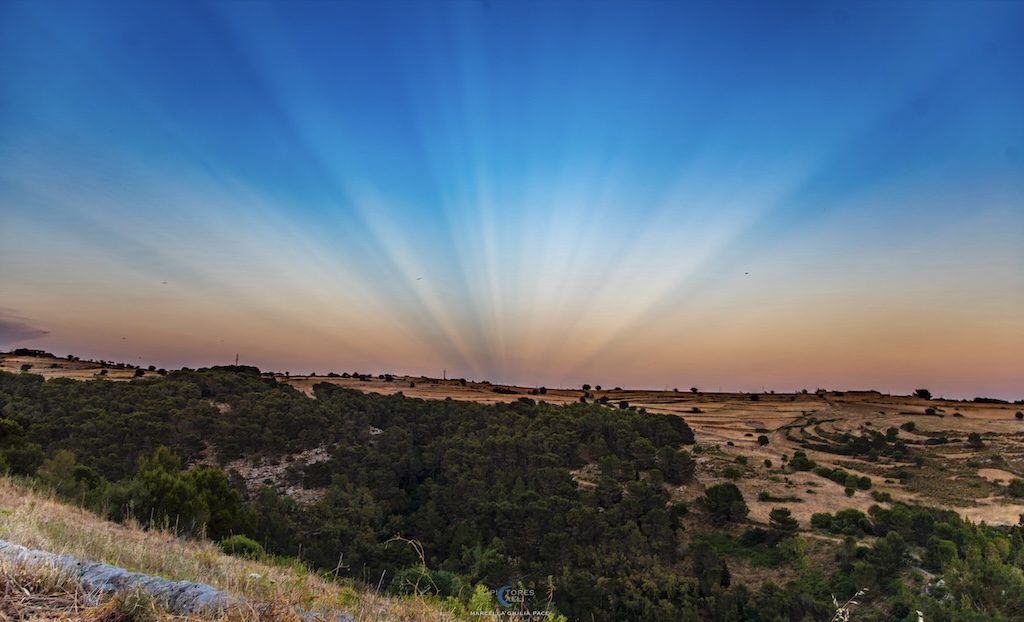 A landscape with an open horizon shows
	    sunset color and coverging rays of light.
