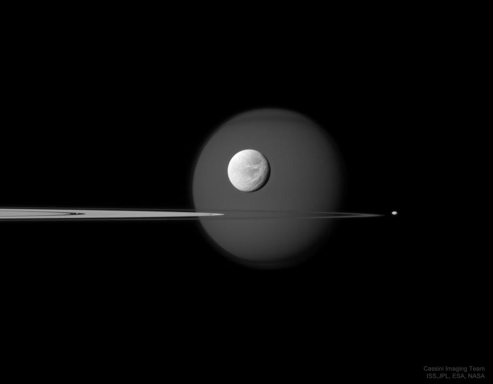 Saturn's rings are pictured, nearly sideways, along with four of Saturn's moons. See Explanation.