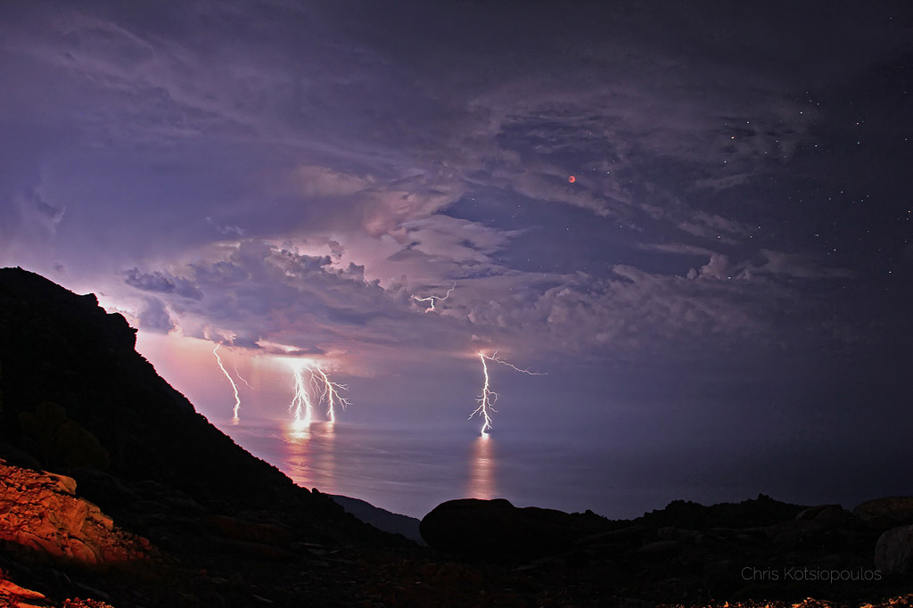 A total lunar eclipse with lightning in the foreground as seen from Greece.
Please see the explanation for more detailed information.