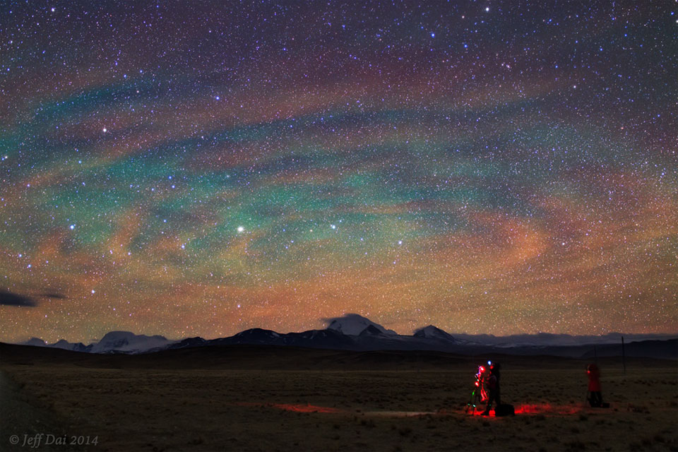The featured image shows a dark field with a photographer
lit in red imaging a night sky tinged with green airglow and
decorated with clouds that appear collectively like a giant
spiral.
Please see the explanation for more detailed information.