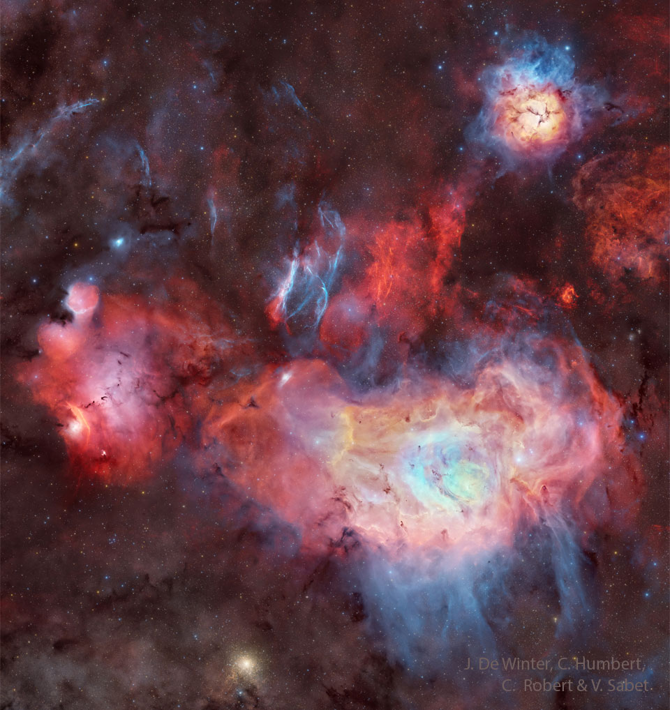 A starfield surrounds a several large nebulas
that appear mostly red but also white and blue.
Dark dust and blue filaments also populate the frame. 
Please see the explanation for more detailed information.
