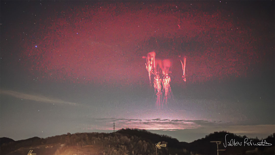 Trees on a hilltop are seen in a starry sky but with
clouds on the far horizon. A strange red circular band of 
light is seen in the sky. Near this band's center, some
bright jellyfish like structures are visible. 
Please see the explanation for more detailed information.