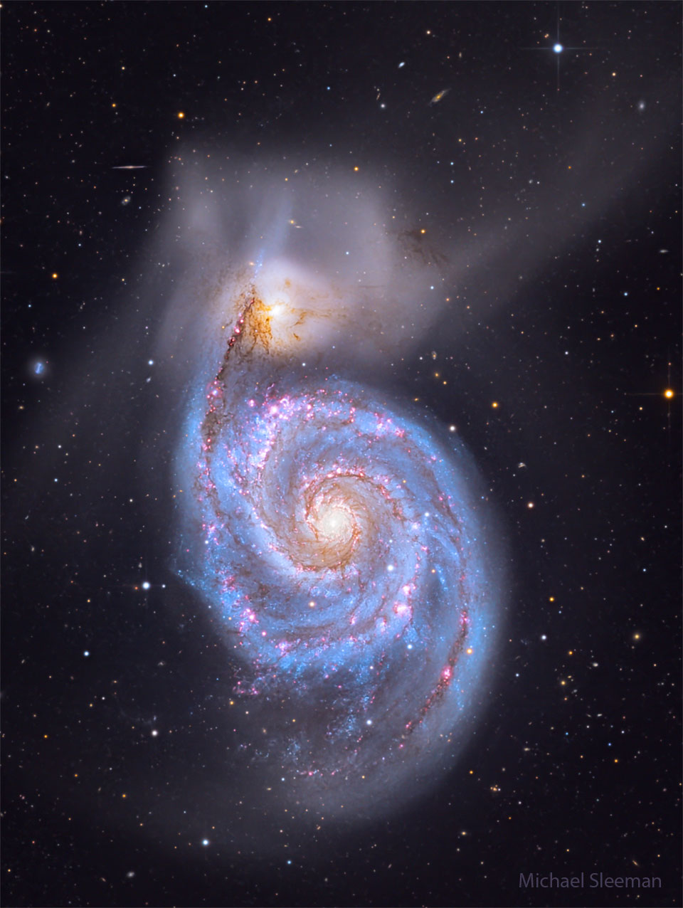 A big spiral galaxy fills the frame, complete with blue
spiral arms dotted with red dust and nebulas. Above the 
spiral galaxy is another more diffuse galaxy that has
faint wisps extending in many directions. 
Please see the explanation for more detailed information.