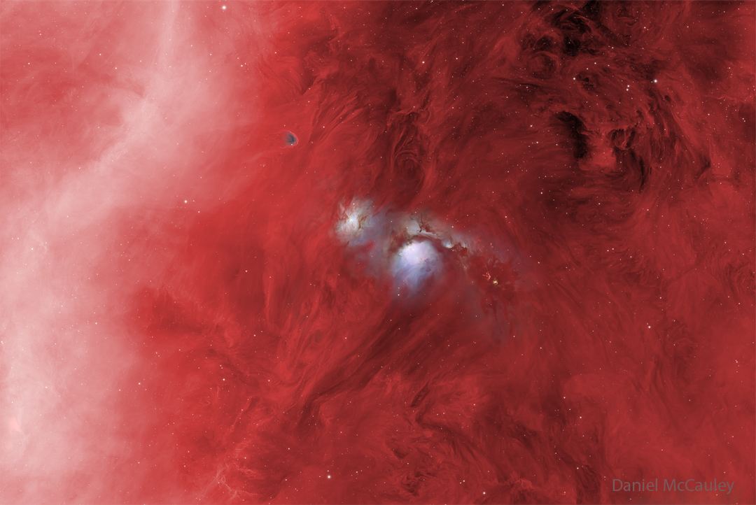 In a starfield glowing red, several features stand
out. On the right is a diffuse white band, and on the 
upper right is some dark dust. Most prominently, though,
are two blue structures in the center, one of which has
a dark band running across near the middle. 
Please see the explanation for more detailed information.