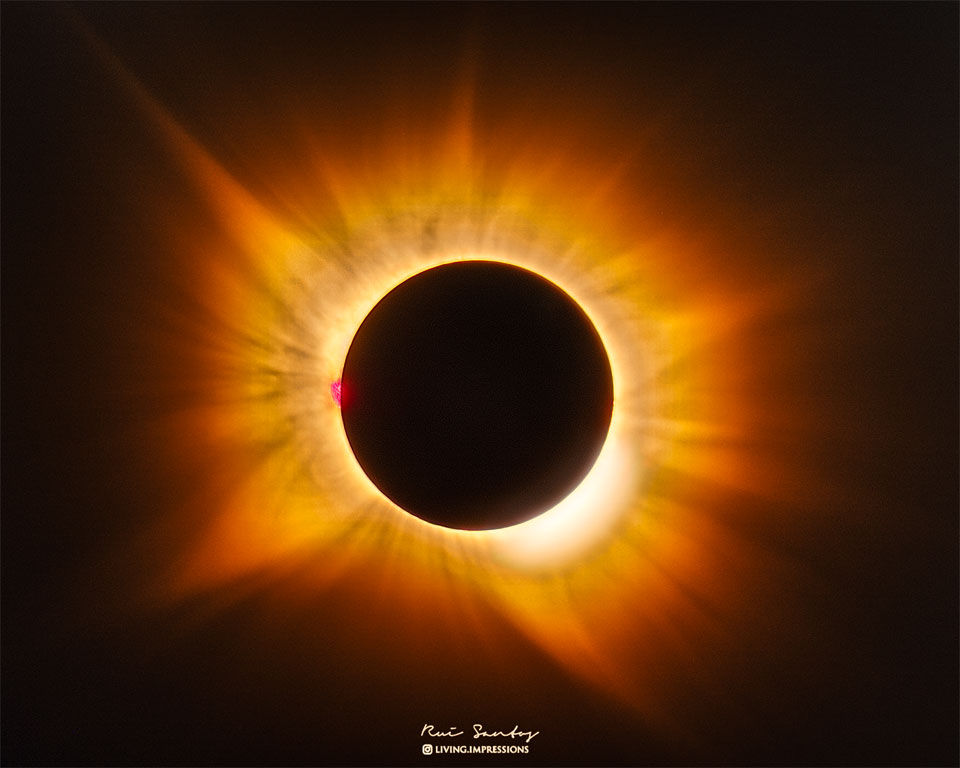 A total eclipse Sun is featured in the image center.
Around the Sun is a filamentary gold-hued corona flowing
out in all directions. 
Please see the explanation for more detailed information.